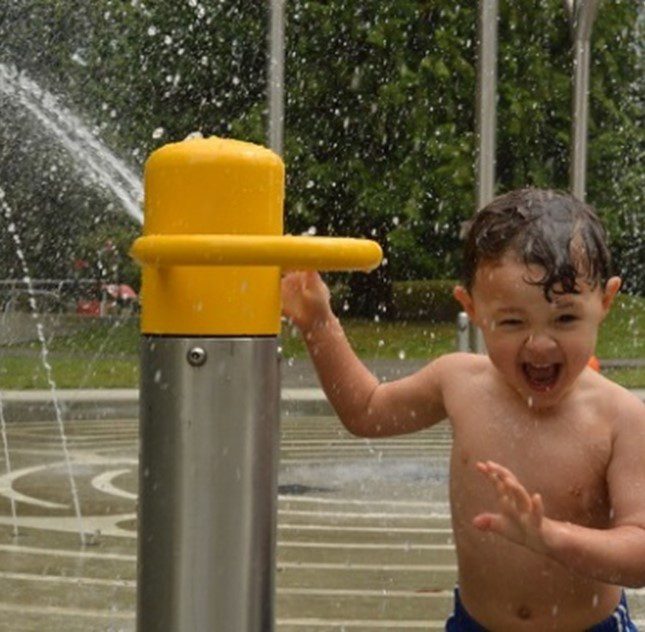 A child smiles and plays at a Seattle Parks spray park feature.