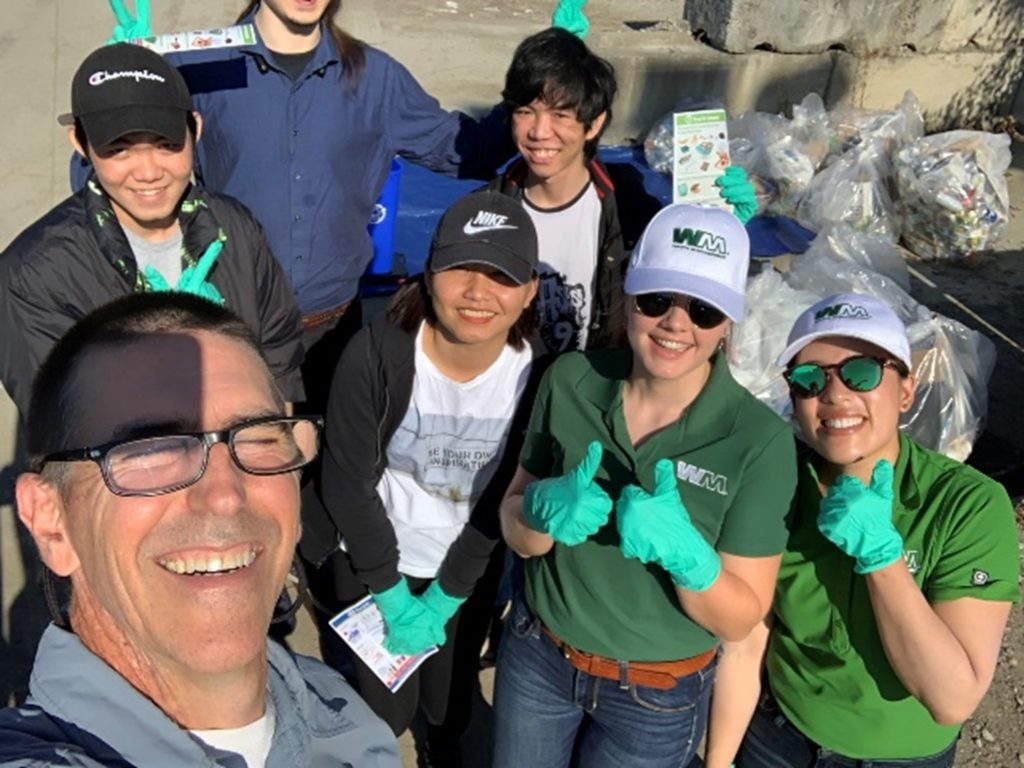 Seattle Parks and Recreation staff pose with 6 Waste Management staff smiling on a sunny day. 