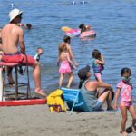 Lifeguard sitting ona stool looking out at the water on a sunny day surrounded by kids