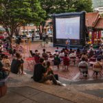 People sitting outside watching a movie projected on a large screen