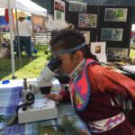 A girl lookign through a microscope at an outdoor environmental education event.