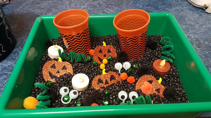 An assortment of Halloween themed craft trinkets in a bin of coffee beans.