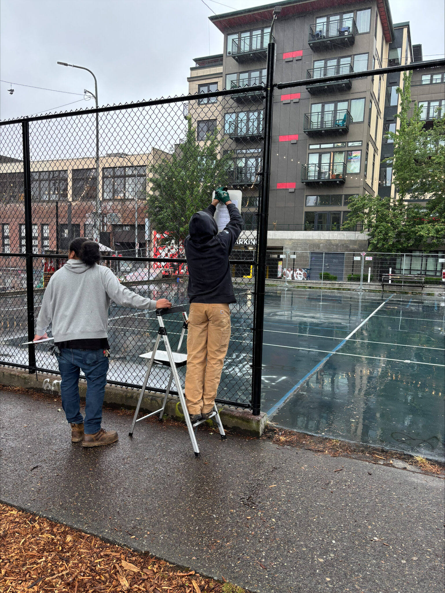 Workers posting a sign on a fence around a court