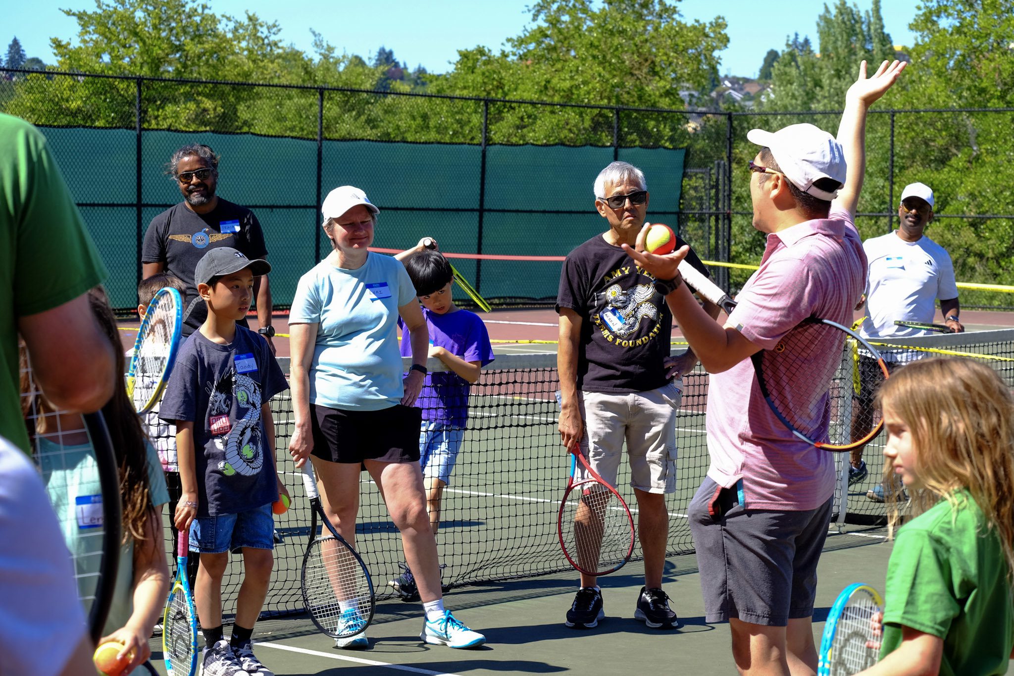 Children playing tennis outdoors at a tennis clinic gathered in a group learning